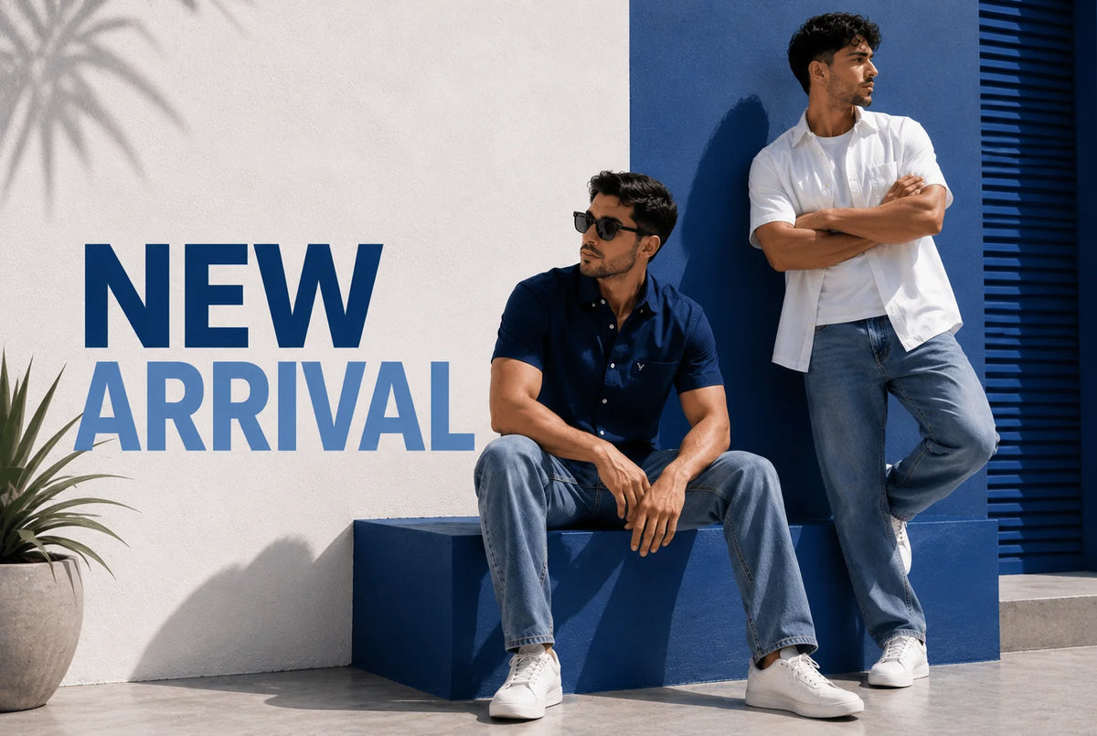 Two men modeling casual clothing in an outdoor setting with a white and blue wall. One man sits on a blue block wearing a navy polo shirt and light blue jeans, while the other stands wearing a white button-up shirt and light blue jeans.