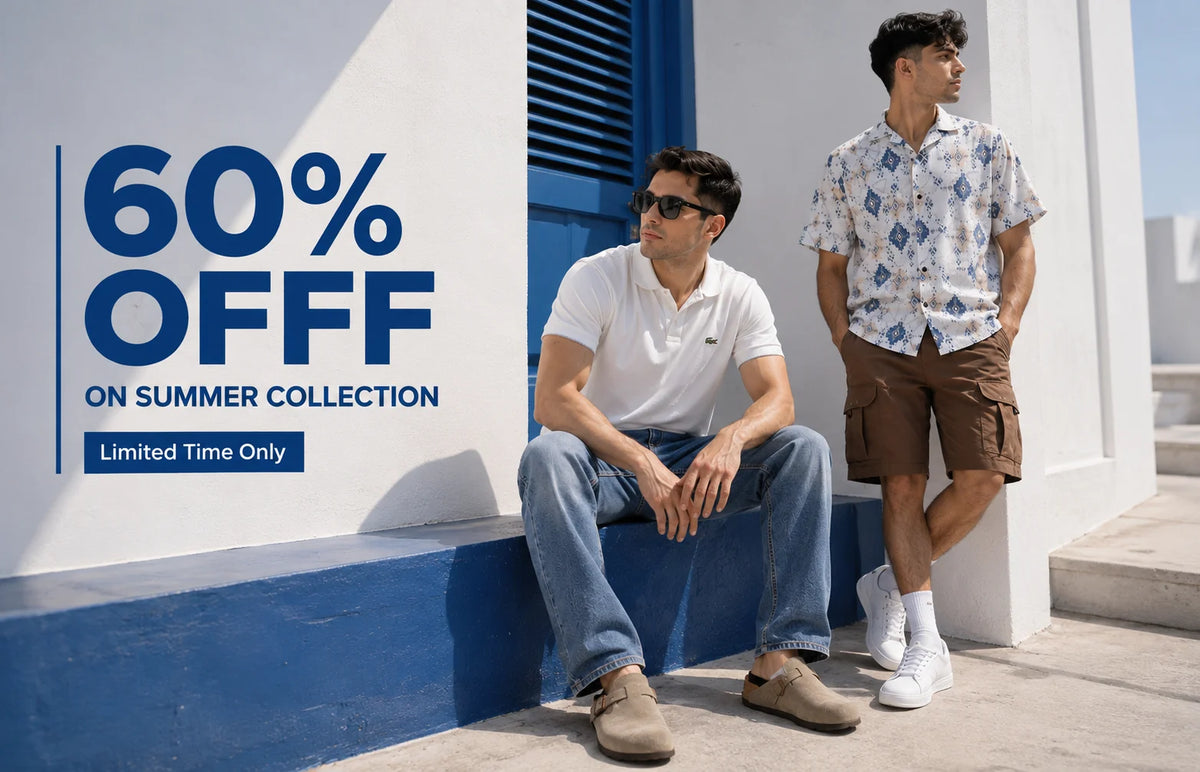 Two men modeling summer clothing in front of a white wall with blue trim. One man sits on a blue ledge wearing a white polo shirt and blue jeans, while the other stands wearing a white short-sleeve button-up shirt with a blue pattern, brown cargo shorts, and white sneakers.