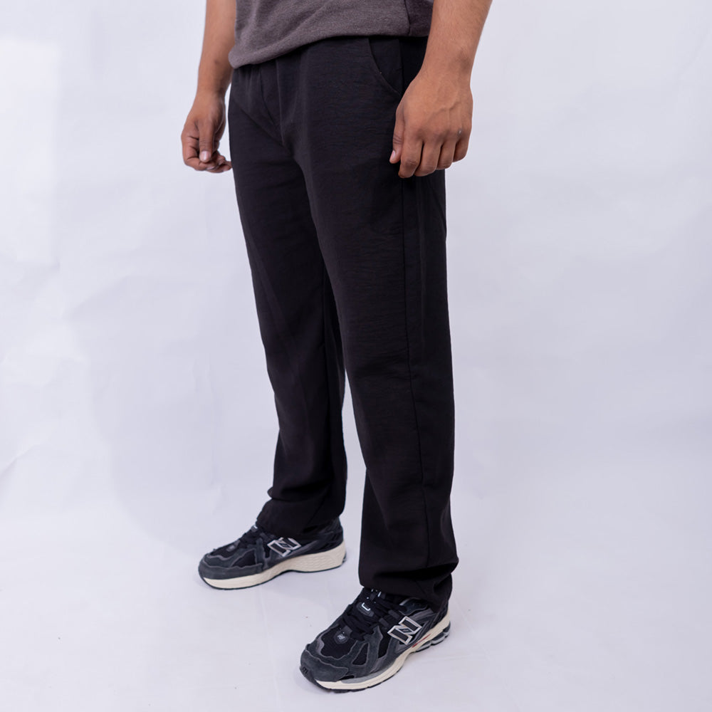A person wearing black jogger-style pants with side pockets and black sneakers, shown from the waist down against a plain light gray studio background.