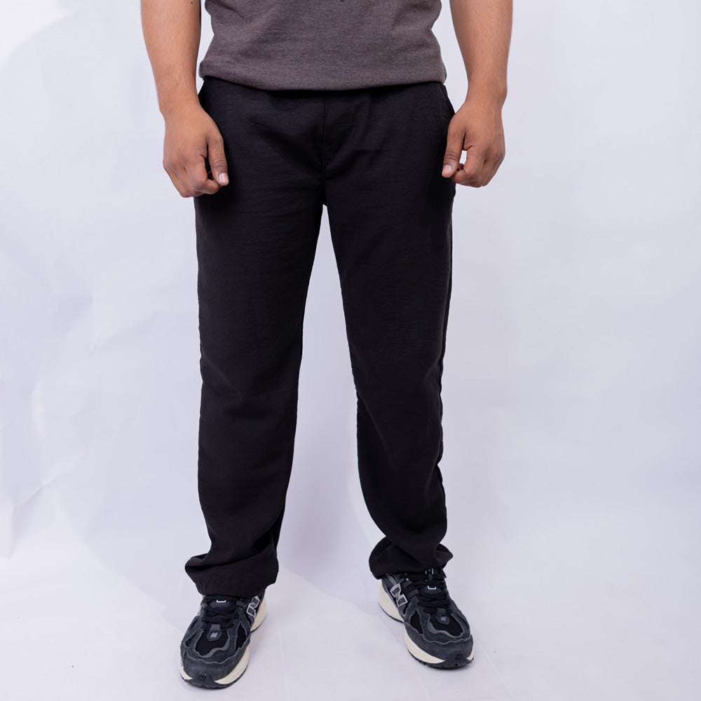 A person wearing black straight-leg sweatpants, a gray t-shirt, and black sneakers, standing against a light gray studio background.