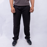 A person wearing black straight-leg sweatpants, a gray t-shirt, and black sneakers, standing against a light gray studio background.